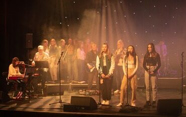 A photograph from a previous Teenage Theme Night of three girls singing on the Hawk's Well stage