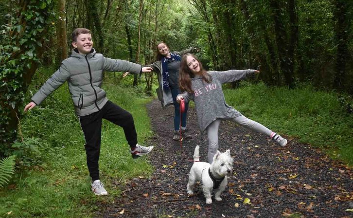 A woman, a dog and two children standing on one foot in a forest