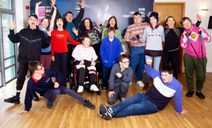 Young people with disabilities stand and wave for a photo in the theatre's atrium