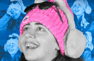 A photograph of a girl smiling and looking up. She's wearing a pink hat, earmuffs and sunglasses on top of her head