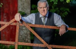 A photograph of Mikel Murfi leaning on a wooden fence