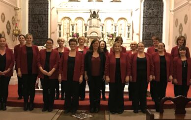 A photograph of the Coolaney Gospel Choir. They are all dressed in black pants and shirts, with dark red suit jackets over their shirts. They are standing in front of the altar in a church. 