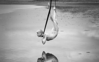 A black and white photograph or Aisling Ni Cheallaigh in an acrobatic pose above water