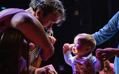 A photo of a baby looking up at a guitar player