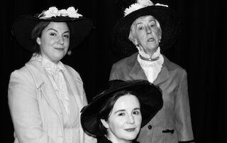 A black and white photograph of three actresses dressed in suffragette era clothing