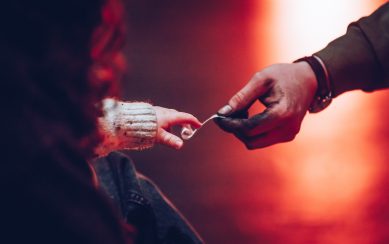 Adult hand handing over a slip of paper to a toddler's hand with an orange background 