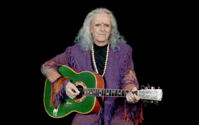 Performing artist Donovan wearing a purple jacket and holding a green guitar 