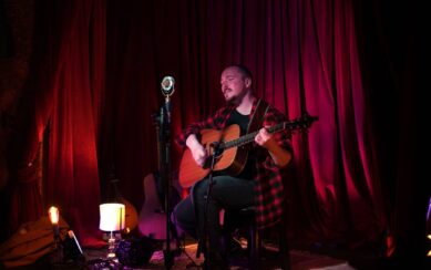 Musician playing guitar against a red curtain 