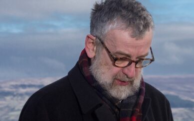 Man with glasses staring at the ground against a blue sky