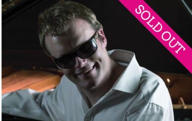 Artist Derek Paravicini sitting at his piano wearing sunglasses