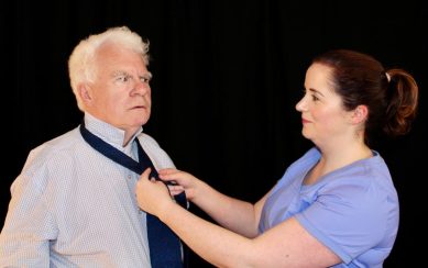 A nurse ties a tie for a puzzled inspector.