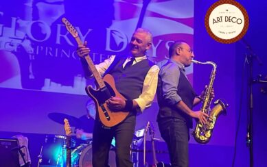 A band performs on a purple-lit stage in front of a "Glory Days" backdrop. A guitarist and a saxophonist stand back-to-back in the foreground.