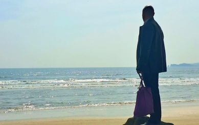Silhouette of a man standing on some rocks staring out at the sea 