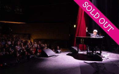Pianist on stage under spotlight waving at audience