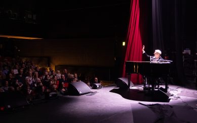 Pianist on stage under spotlight waving at audience