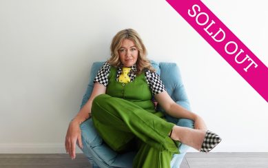 Comedian Serena Terry sitting on a chair wearing green against a white wall