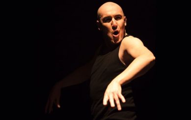 Pat Kinevane on stage, set against a black backdrop