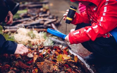 Child wearing a red raincoat holding a magnifying glass to some soil and leaves on the ground Child wearing a red raincoat holding a magnifying glass to some soil and leaves on the ground