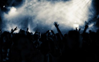 A photograph of a lit stage filled with smoke and a silhouette of a crowd in front of it A photograph of a lit stage filled with smoke and a silhouette of a crowd in front of it
