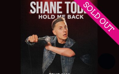 Shane Todd with a microphone against a black background