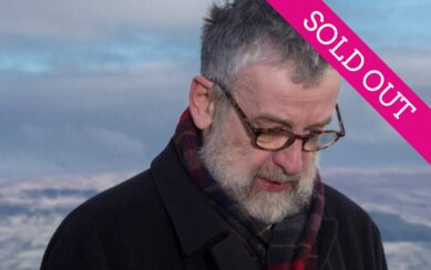 Man with glasses staring at the ground against a blue sky