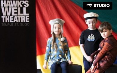 Kids dressed up in front of a colorful flag and next to a Hawk's Well banner