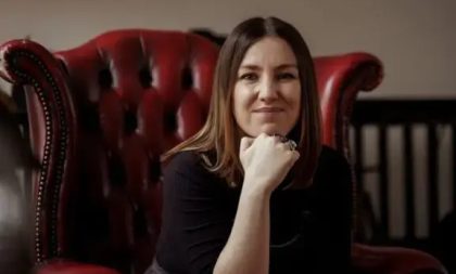 A photograph of Clare Monnelly sitting in a maroon leather chair. A photograph of Clare Monnelly sitting in a maroon leather chair.