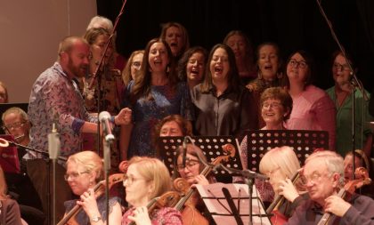 A photograph of musicians and a choir on the Hawk's Well stage. A photograph of musicians and a choir on the Hawk's Well stage.