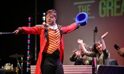 A young man wearing a costume from The Greatest Showman performing on stage