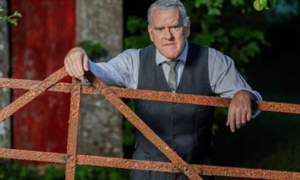 A photograph of Mikel Murfi leaning on a wooden fence