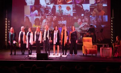 A photograph of performers standing on stage with a collage of photographs projected behind them