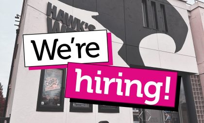 A photograph of the front of Hawk's Well Theatre with a banner stating "We're hiring" across it