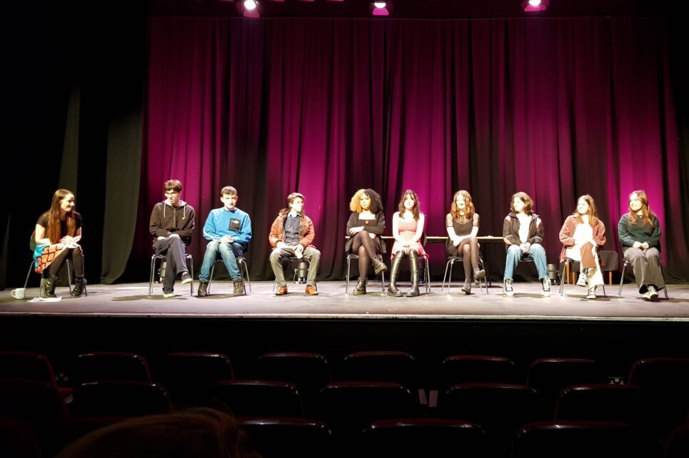 A photograph of the teenage participants of the New Voices programme sitting on the Hawk's Well stage. 