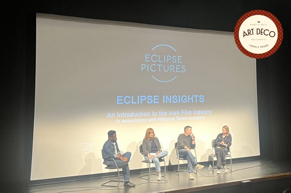 Panel discussion on a theatre stage with cinema screen in the background Panel discussion on a theatre stage with cinema screen in the background
