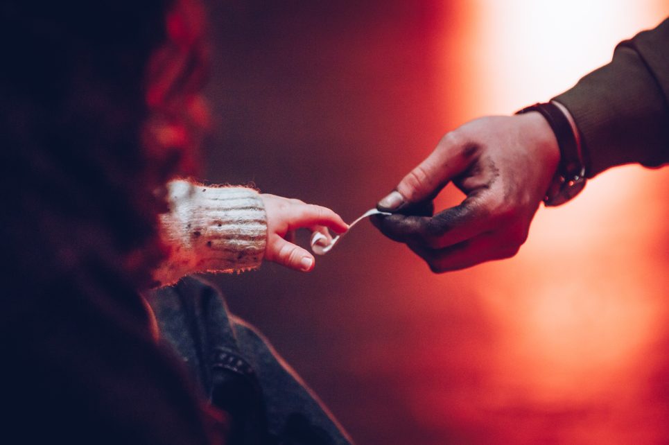 Adult hand handing over a slip of paper to a toddler's hand with an orange background
