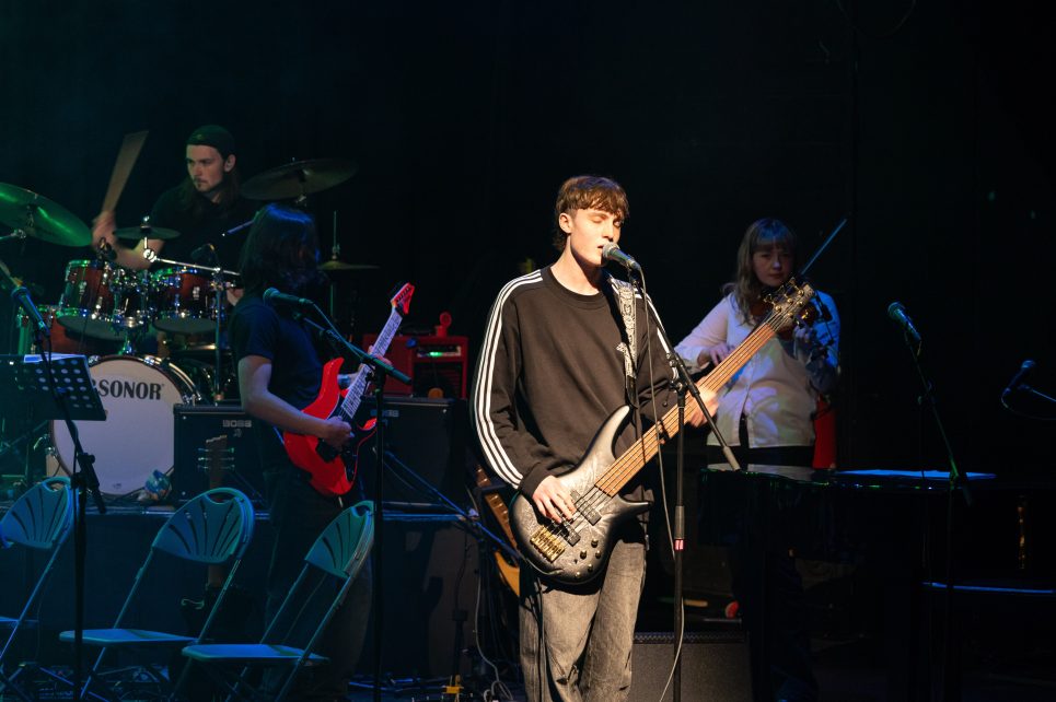 Teenage boy playing an electric guitar on a stage with band behind him Teenage boy playing an electric guitar on a stage with band behind him