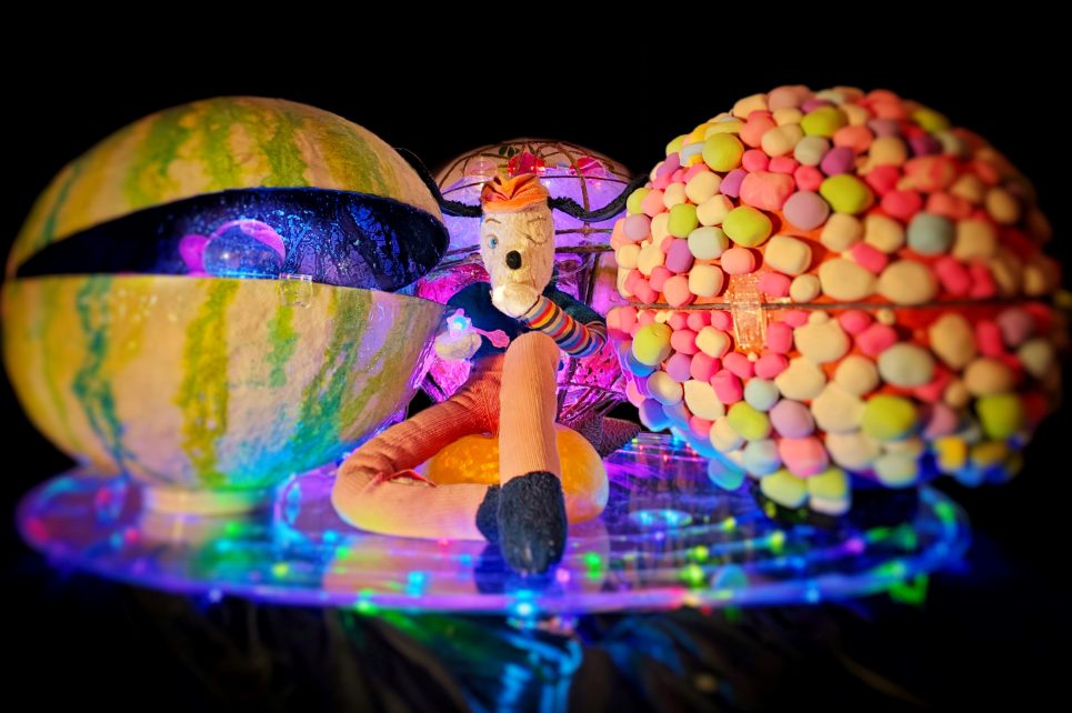 Colourful teddy bear sitting next to colourful plastic orbs