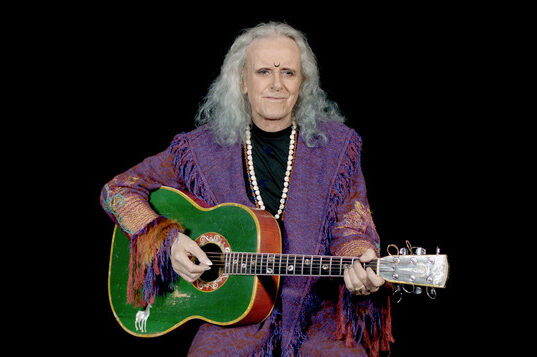 Performing artist Donovan wearing a purple jacket and holding a green guitar