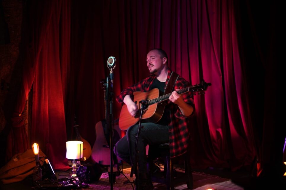 Musician playing guitar against a red curtain