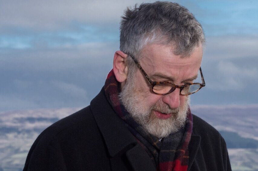 Man with glasses staring at the ground against a blue sky