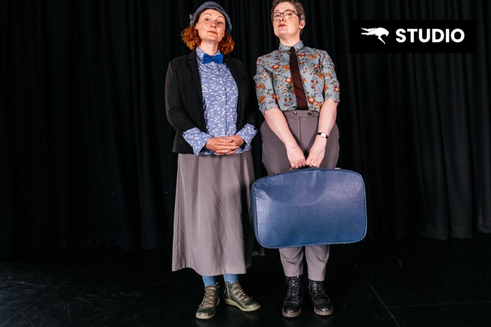 Two women standing against a black background 