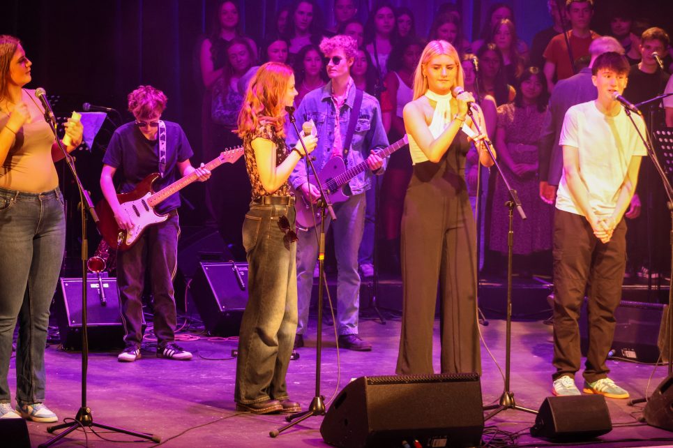 Teenagers performing on a purple lit stage with various instruments and microphones