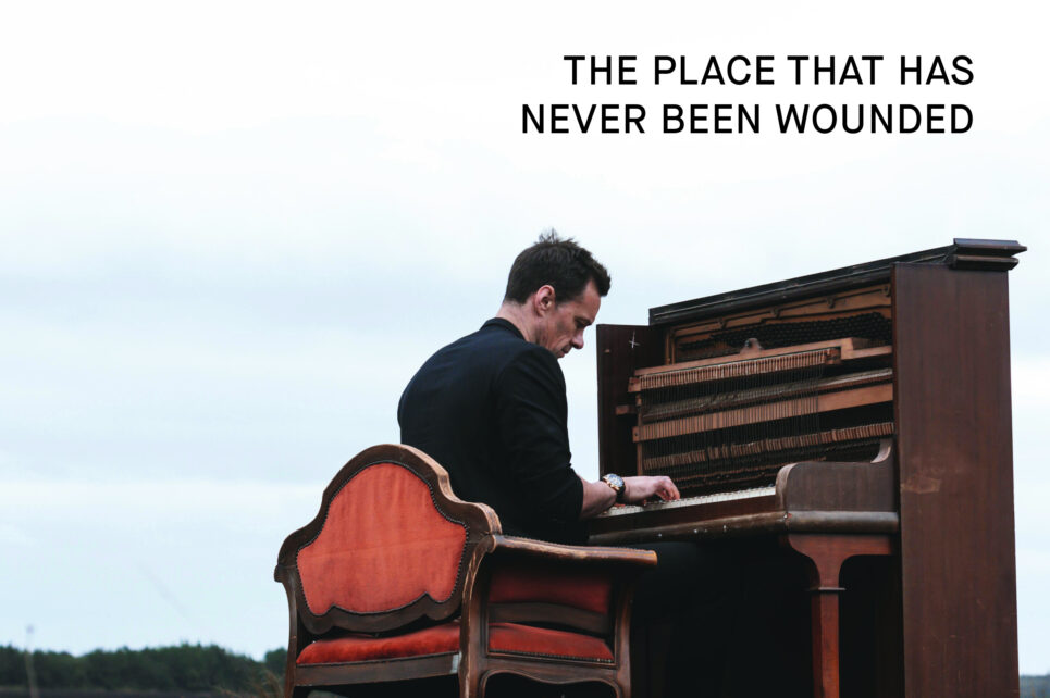 Artist Niall Breslin sitting at a piano in a rural landscape 