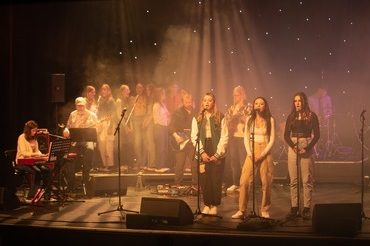 A photograph from a previous Teenage Theme Night of three girls singing on the Hawk's Well stage