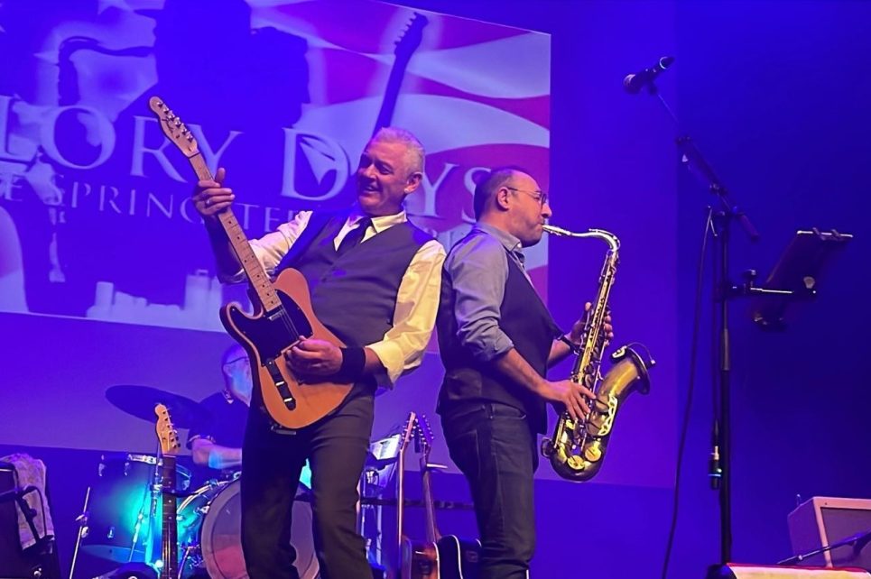 A guitar and a saxophone player standing back to back on a stage performing A guitar and a saxophone player standing back to back on a stage performing