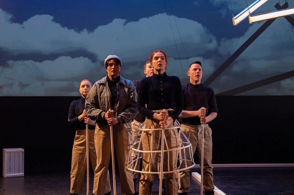 Five cast members from Curious Case of Albert Cashier in light-coloured pants and dark shirts. Each cast member is holding a wooden pole in front of them and they are looking into the distance.