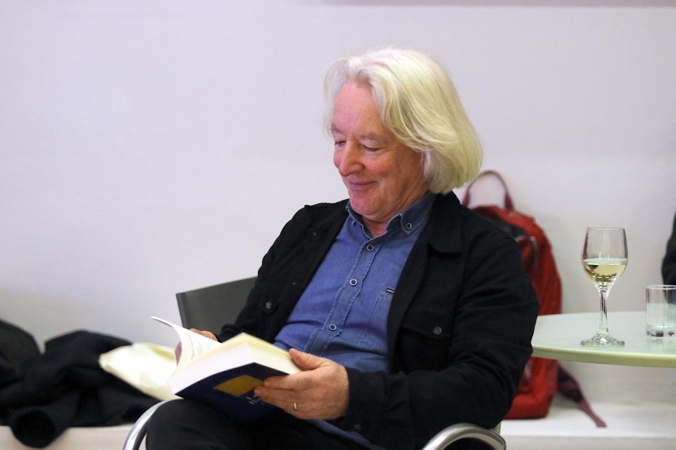 A photograph of Brian Leyden reading a book and smiling A photograph of Brian Leyden reading a book and smiling