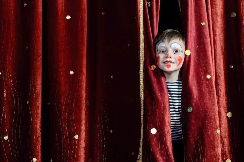 young boy in clown costume and make up peaking from behind a stage curtain young boy in clown costume and make up peaking from behind a stage curtain
