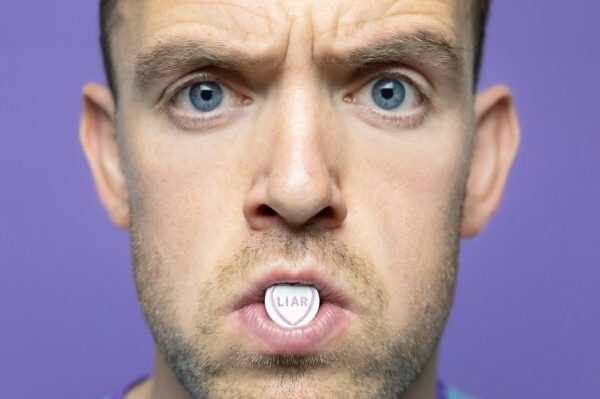 A photograph of Tom Moran holding a Love Heart with the word Liar in his mouth
