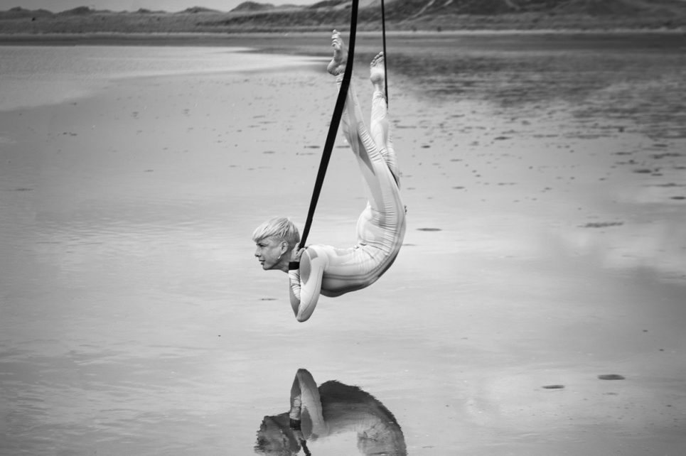 A black and white photograph or Aisling Ni Cheallaigh in an acrobatic pose above water